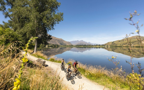 People biking along trail next to lake near Arrowtown in Queenstown, New Zealand