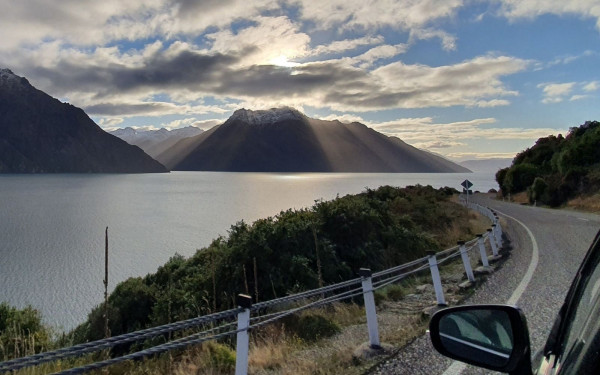 Car driving on mountain road next to lake in Queenstown, New Zealand